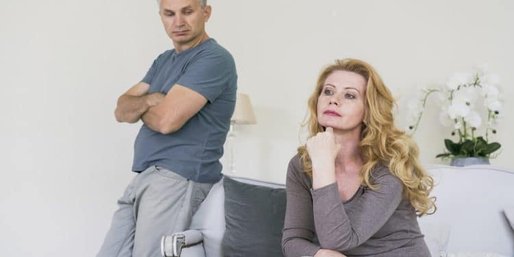 Homem de braços cruzados observa mulher sentada, ambos sérios em sala clara, simbolizando as frases que revelam que o respeito terminou.