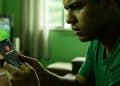 Homem acompanha jogo de futebol enquanto recebe alerta de possível golpe no celular.
