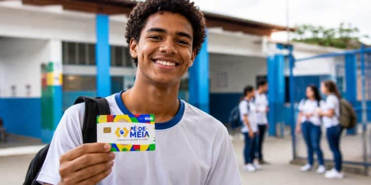 Estudante do ensino médio público segurando cartão do Pé-de-Meia, programa que paga R$ 200 por mês a quem cumprir 80% de frequência escolar