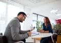 Recrutador analisa currículo diante da candidata, situação em que surgem as mentiras mais comuns em entrevistas de emprego