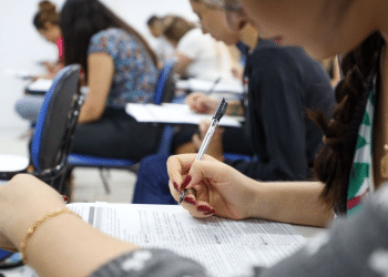 Candidatos realizando prova de concurso público em sala de aula.