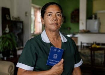 Trabalhadora doméstica de uniforme segura a Carteira de Trabalho e Previdência Social, representando as novas garantias aprovadas para a categoria.