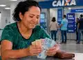 Mulher segurando cédulas em agência da Caixa, representando os pagamentos do Bolsa Família de junho de 2026, com liberação de até R$ 1.000.