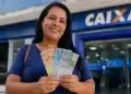 Mulher segura cédulas de reais em frente a uma agência da Caixa, representando pagamento de R$ 1.000 confirmado para 30 de junho.