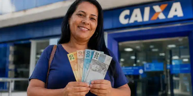 Mulher segura cédulas de reais em frente a uma agência da Caixa, representando pagamento de R$ 1.000 confirmado para 30 de junho.