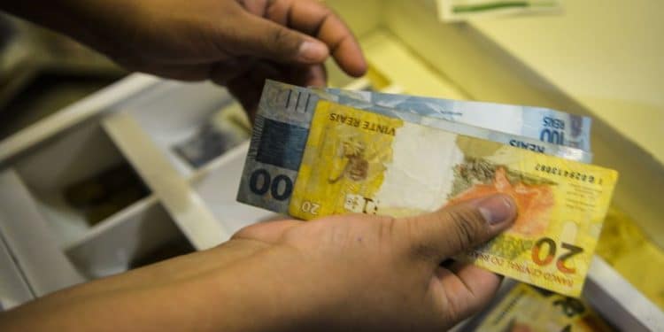 Mãos segurando notas de 20 e 100 reais próximas a caixa registradora aberta, simbolizando o pagamento de R$ 4.521,00.