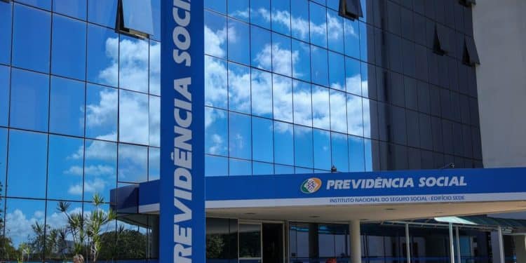 Fachada espelhada do prédio do INSS com letreiros Previdência Social e mulher caminhando, simbolizando o pagamento do valor de R$ 8.475,55, atual teto do INSS.