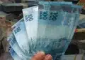 Mão segurando cédulas de R$ 100 em destaque, simbolizando a liberação de pagamento de R$ 2.621 em 1º de julho.