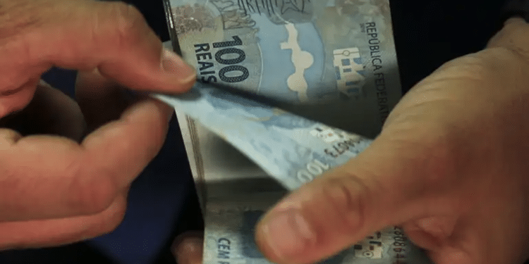 Mãos contam maço de cédulas de cem reais em close