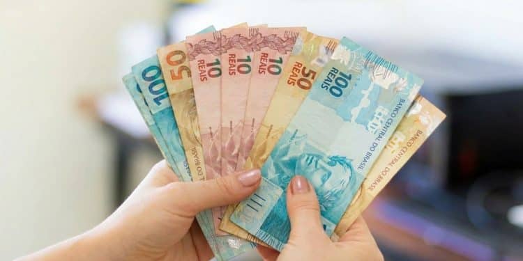 Mãos segurando notas de 10, 50 e 100 reais em leque