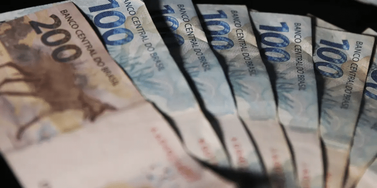 Leque de cédulas de cem e duzentos reais sobre fundo escuro