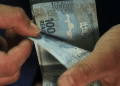 Pessoa conta notas de R$ 100 ao receber os pagamentos liberados para desempregados em 2026