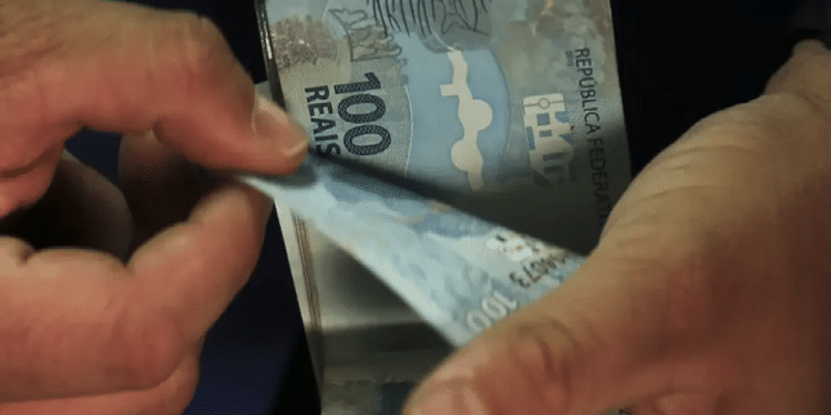 Pessoa conta notas de R$ 100 ao receber os pagamentos liberados para desempregados em 2026