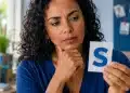 Mulher observando um cartão com a letra “S” enquanto reflete sobre uma regra de português, representando uma palavra em que o plural aparece no meio.