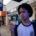 Estudante de uniforme observa o cartão do Pé-de-Meia em frente a uma agência da CAIXA, representando as dúvidas sobre o saque dos incentivos do programa.
