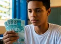 Estudante do ensino médio segurando notas de R$ 100, mostrando o pagamento do programa Pé-de-Meia de junho de R$ 1.000.