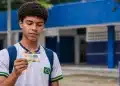 Estudante segura cartão do Pé-de-Meia em frente a uma escola pública, representando a dúvida sobre quem recebe o benefício em junho.
