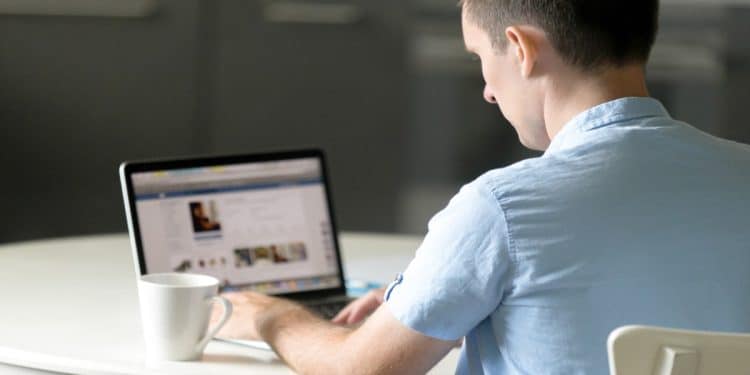 Homem sentado à mesa usa o laptop para acessar e atualizar o perfil no LinkedIn