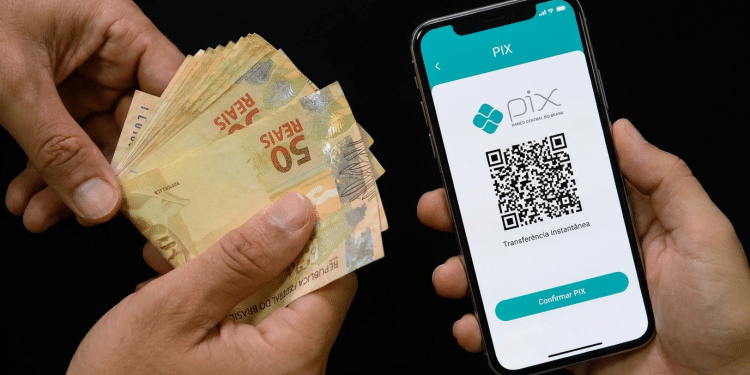 Mãos segurando notas de real e celular exibindo QR Code do PIX Banco Central, simbolizando o Pix automático de R$ 1.000 do Imposto de Renda.