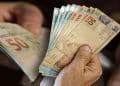 Mãos seguram notas de real representando a restituição de até R$ 1.000 paga via Pix pela Receita Federal