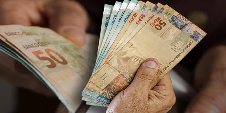 Mãos seguram notas de real representando a restituição de até R$ 1.000 paga via Pix pela Receita Federal