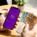 Alt text: Pessoa segurando celular com aplicativo do Nubank e notas de R$ 100 e R$ 50.