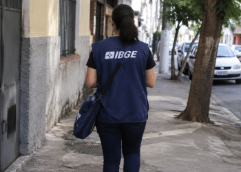 Recenseadora do IBGE caminhando em rua urbana, representando seleção com 8.238 vagas de nível médio.