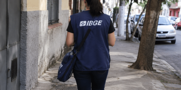 Recenseadora do IBGE caminhando em rua urbana, representando seleção com 8.238 vagas de nível médio.