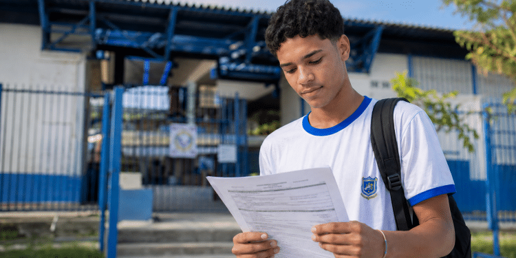 Estudante jovem lendo documento de inscrição em frente a uma escola pública, representando processo seletivo do Instituto Federal.