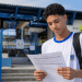Estudante jovem lendo documento de inscrição em frente a uma escola pública, representando processo seletivo do Instituto Federal.