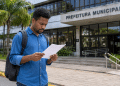 Homem lê documento em frente à Prefeitura Municipal durante processo seletivo para Agente Comunitário de Saúde.