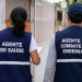 Agente de saúde e agente de combate às endemias fardados de costas durante atendimento em área residencial.