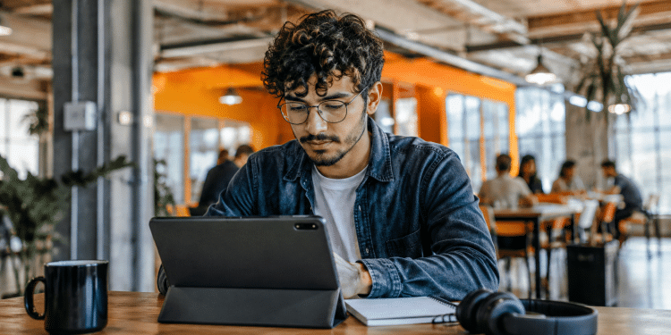 Jovem usando tablet em coworking moderno, representando preparação para profissões do futuro e novas tendências do mercado de trabalho.