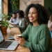 Mulher sorrindo trabalhando em laptop em café, simbolizando profissões flexíveis e renda extra.