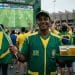 Vendedor ambulante com bandeira do Brasil e bandeja de chope em frente a telão durante a Copa do Mundo, representando as profissões que lucram com o torneio.