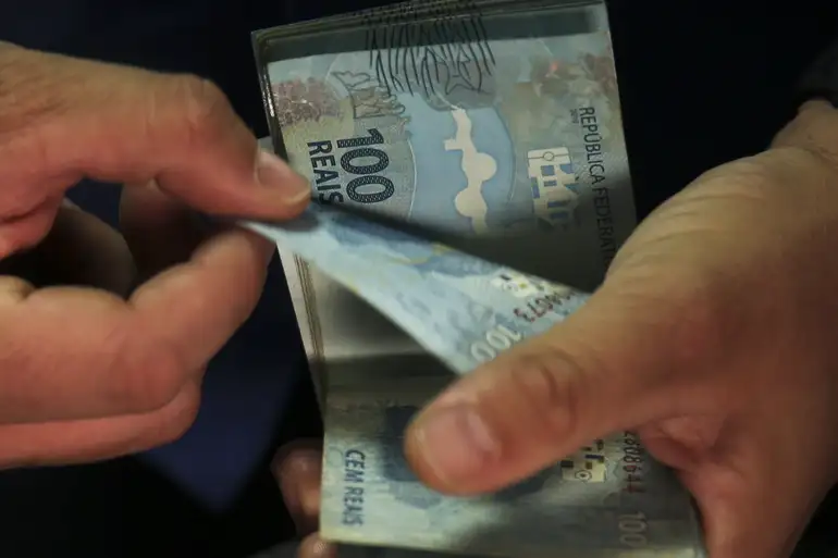 Pessoa conta cédulas de cem reais com as duas mãos.