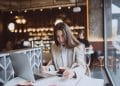 Mulher estuda com notebook e caderno enquanto toma café em uma cafeteria