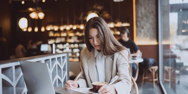 Mulher estuda com notebook e caderno enquanto toma café em uma cafeteria