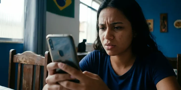 Mulher preocupada olhando para o celular enquanto tenta recuperar o acesso a uma conta online.