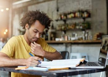Jovem estuda com livro aberto e faz anotações em um caderno sobre a mesa