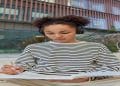 Jovem de fones de ouvido escreve concentrada em um caderno ao ar livre, representando a revisão de regras de português.