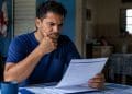 Trabalhador preocupado analisando um documento em casa, representando a conferência das regras e do prazo do seguro-desemprego