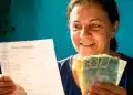 Mulher segura extrato bancário e notas de real após verificar ressarcimento de descontos indevidos do INSS.
