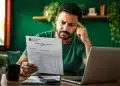 Homem analisando um documento do Imposto de Renda com expressão de preocupação, representando um possível erro nos dados bancários da restituição.