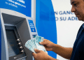 Homem conta cédulas de R$ 100 em frente a caixa eletrônico, representando o saque de até R$ 6.220 do FGTS por calamidade em 2026.