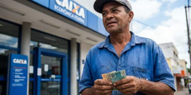 Trabalhador conta cédulas de real em frente a uma agência da Caixa Econômica Federal, banco que paga o Saque Calamidade do FGTS