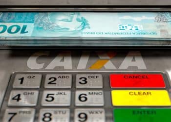 Cédulas de R$ 100 saindo de caixa eletrônico ilustram o Saque Calamidade do FGTS de até R$ 6.220 liberado pela Caixa