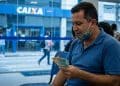 Homem conferindo cédulas de R$ 100 e R$ 50 em frente a uma agência da Caixa, referência ao Saque Calamidade do FGTS