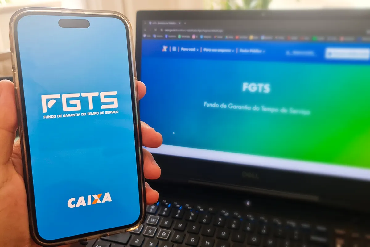 Celular com aplicativo do FGTS aberto ao lado de computador exibindo página do fundo de garantia.