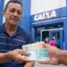 Trabalhador recebendo cédulas de real em frente a uma agência da Caixa, representando o saque de até R$ 1.621 do PIS/Pasep.